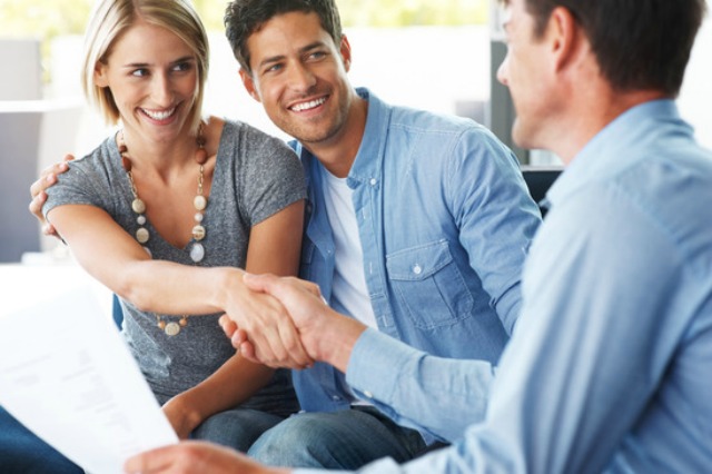 Portrait of a happy young couple shaking hand with financial advisor at home